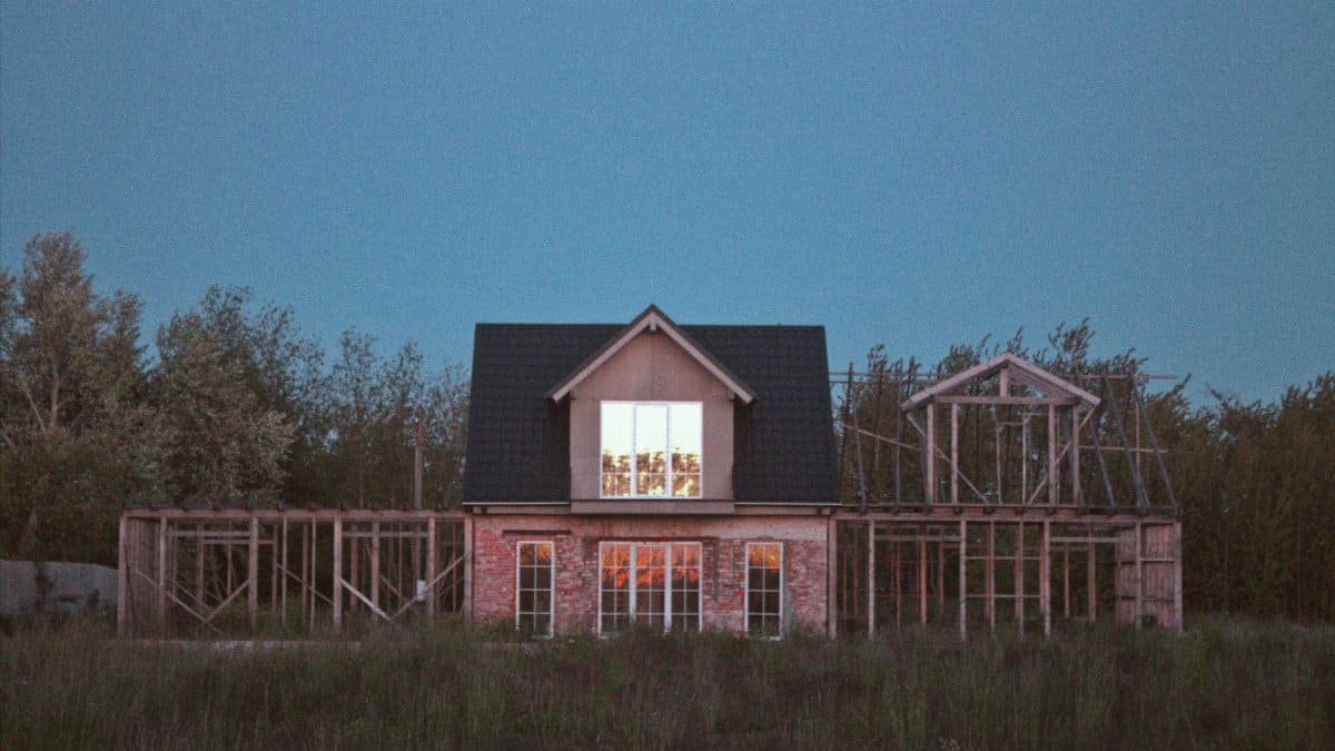 A half-constructed wooden house stands in a field during twilight.