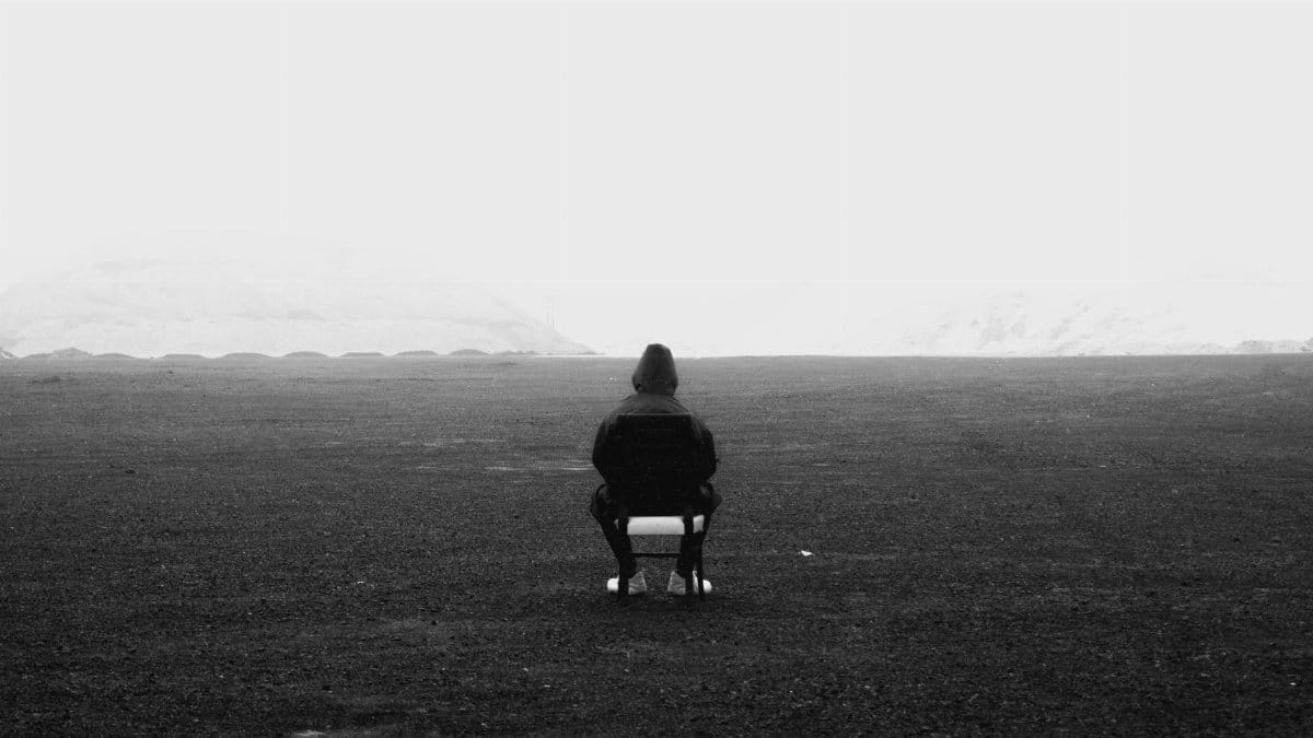 A lone person sitting on a chair in a vast grayscale landscape, evoking solitude.