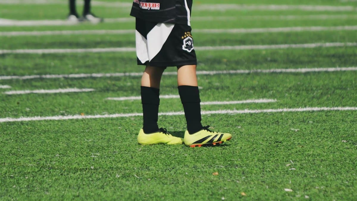 Close-up of a child's legs in soccer gear on a vibrant green football field.