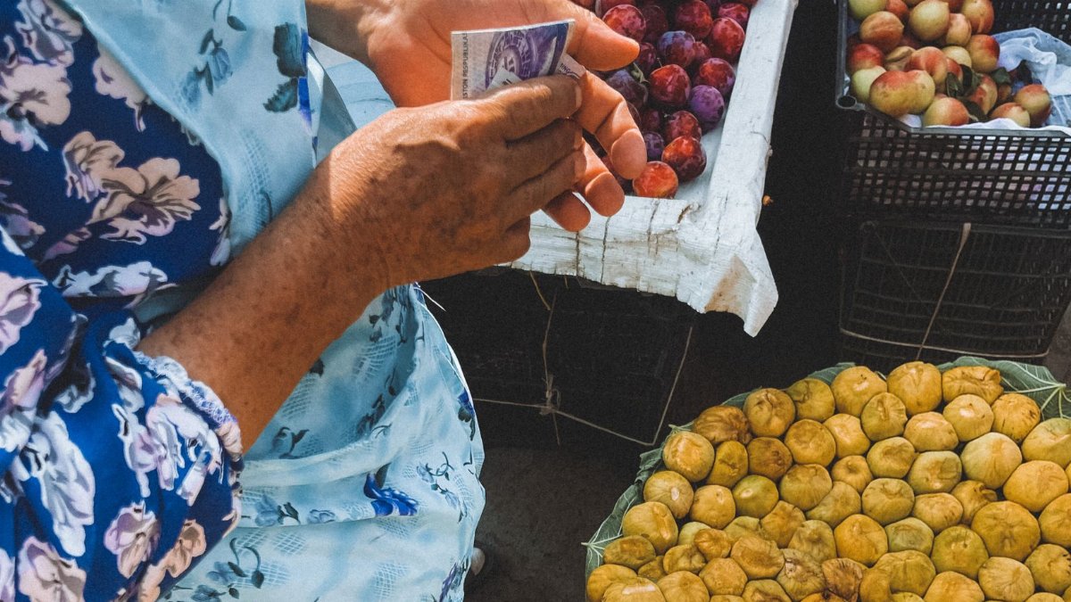 A woman holding money at a vibrant fruit market in Samarkand, Uzbekistan.