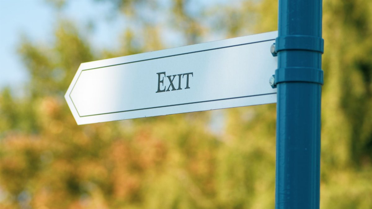 A close-up view of an exit sign mounted on a blue pole in a lush outdoor setting.