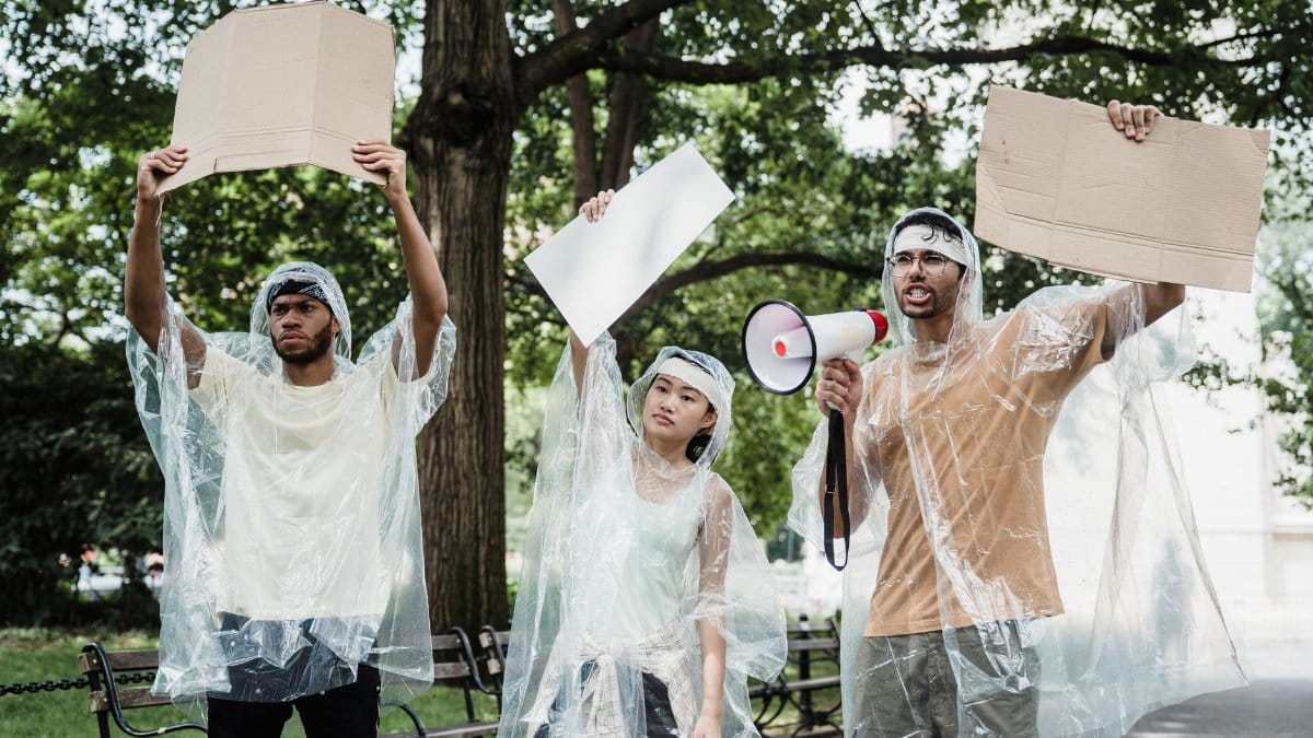Three young activists protest in a park with blank signs and megaphone.