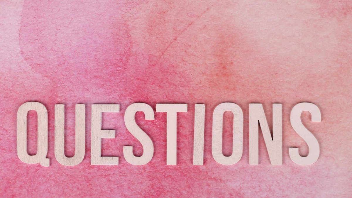 Wooden 'QUESTIONS' text on pink watercolor background, perfect for design and art concepts.