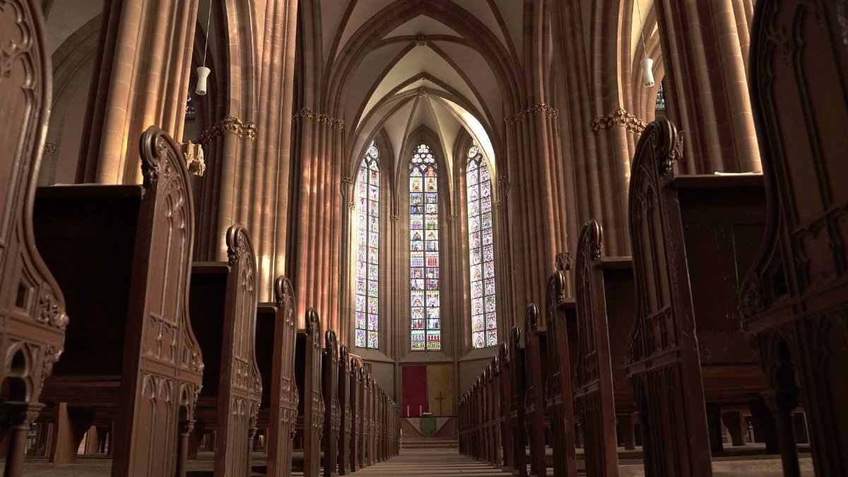 Interior view of a gothic church in Oppenheim, showcasing arches, pews, and stained glass windows.