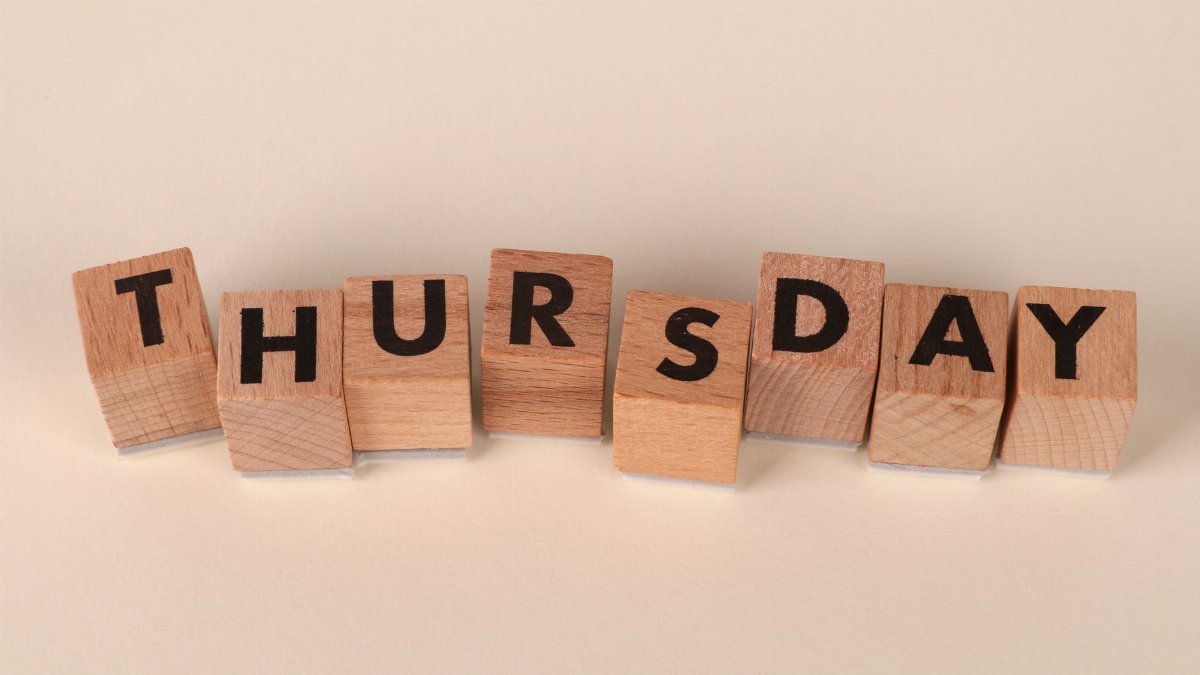 Wooden blocks arranged to spell Thursday on a neutral background.