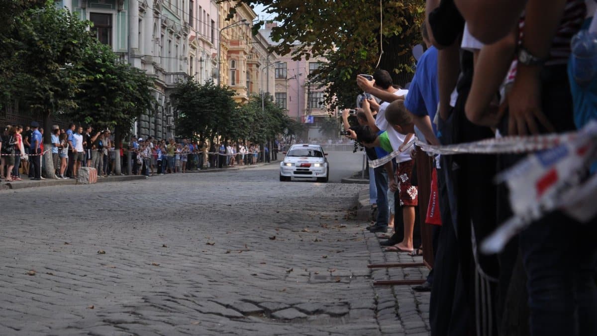 White car speeds down cobblestone street lined with eager spectators during a thrilling city car race.
