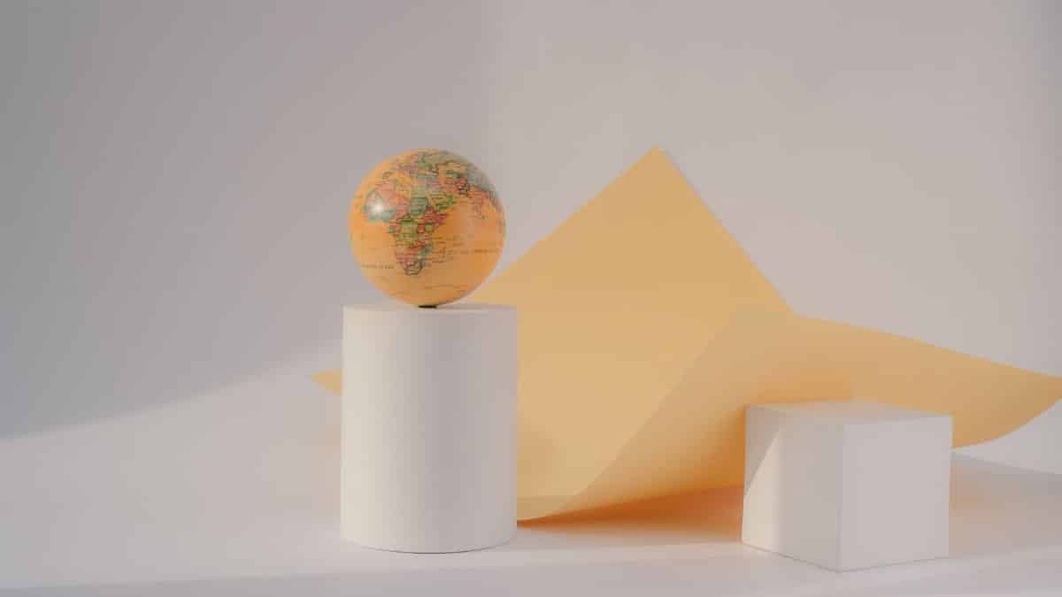 Conceptual still life featuring a globe on geometric white shapes with orange paper.