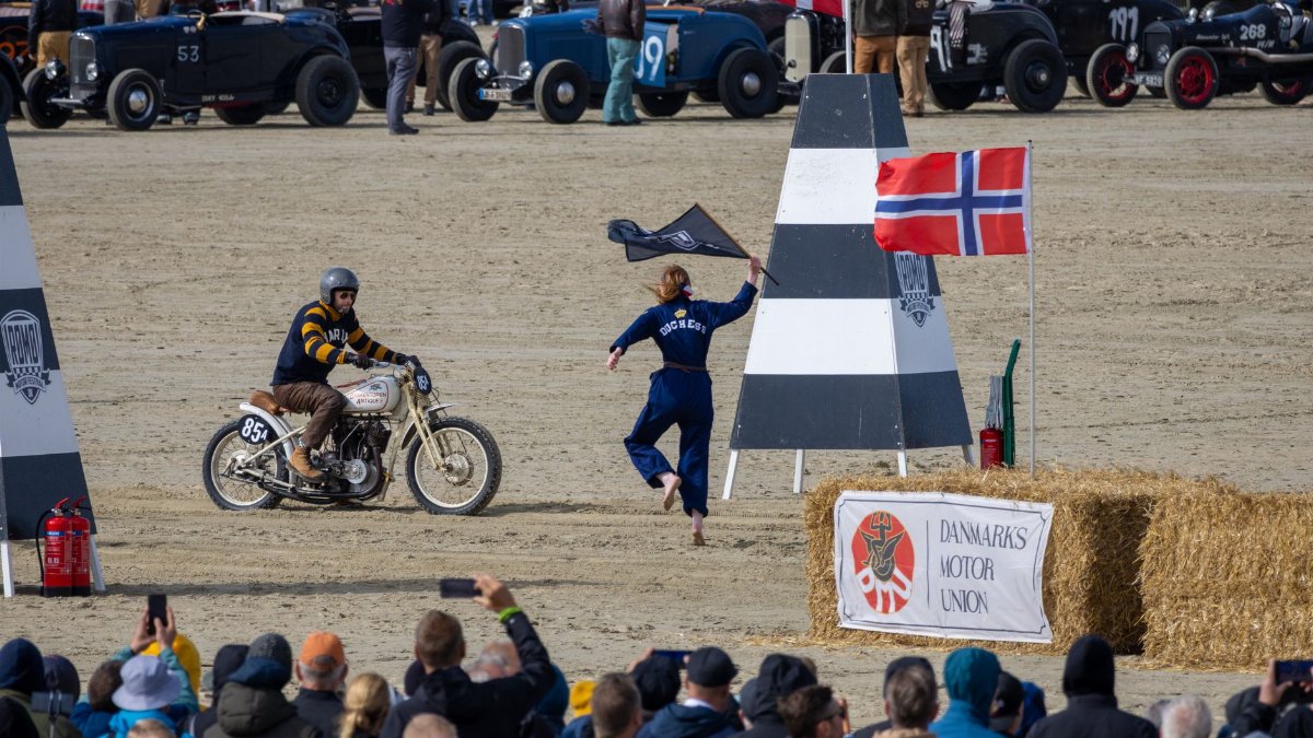 Exciting vintage motorcycle race on a sandy track with spectators in Denmark.