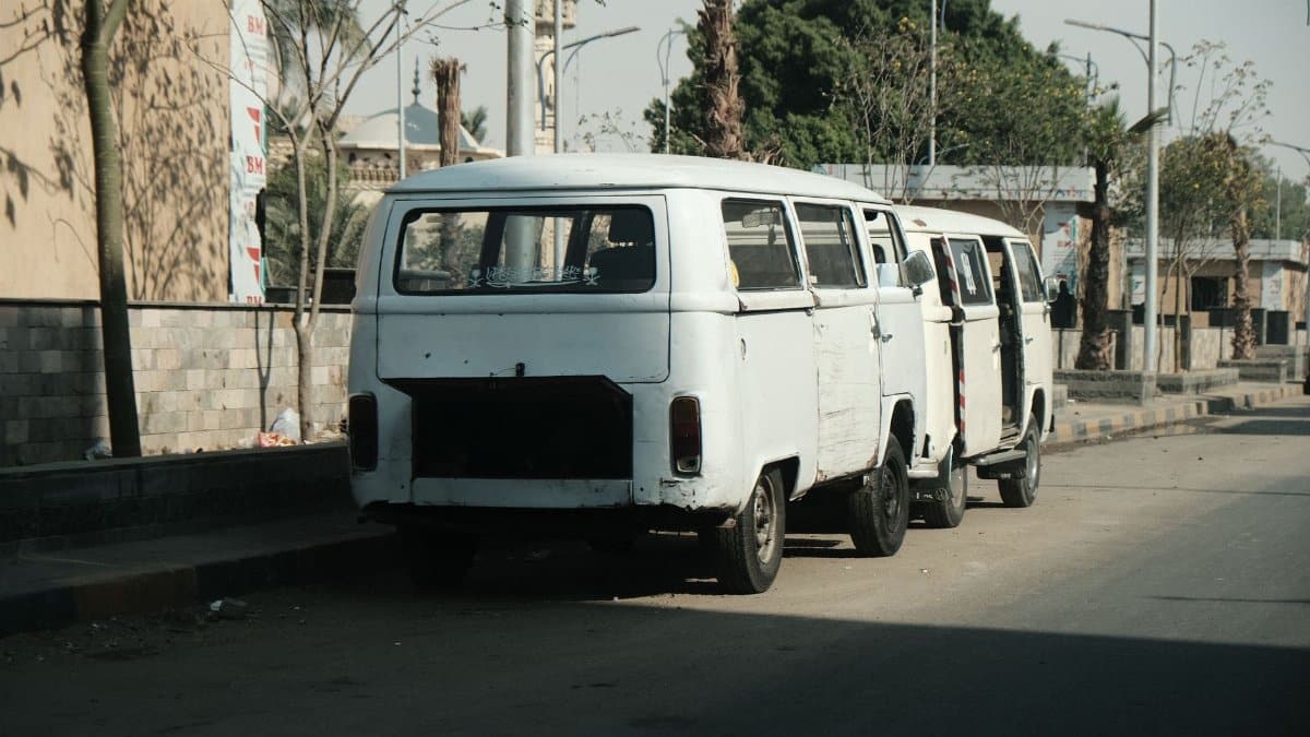 Rustic vintage vans parked in a row on a leafy Cairo street, depicting local transport.