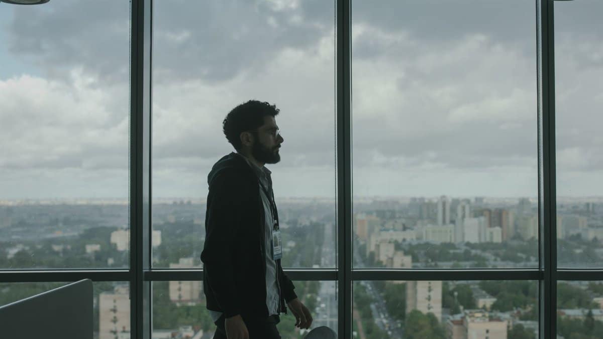 Man in office with vast cityscape view through large windows, moody ambiance.