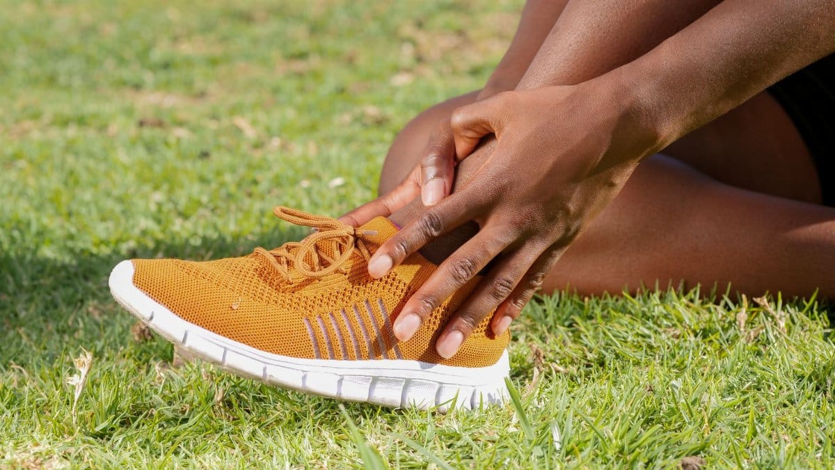 Person holding ankle in orange sneaker, suggesting potential sports injury.
