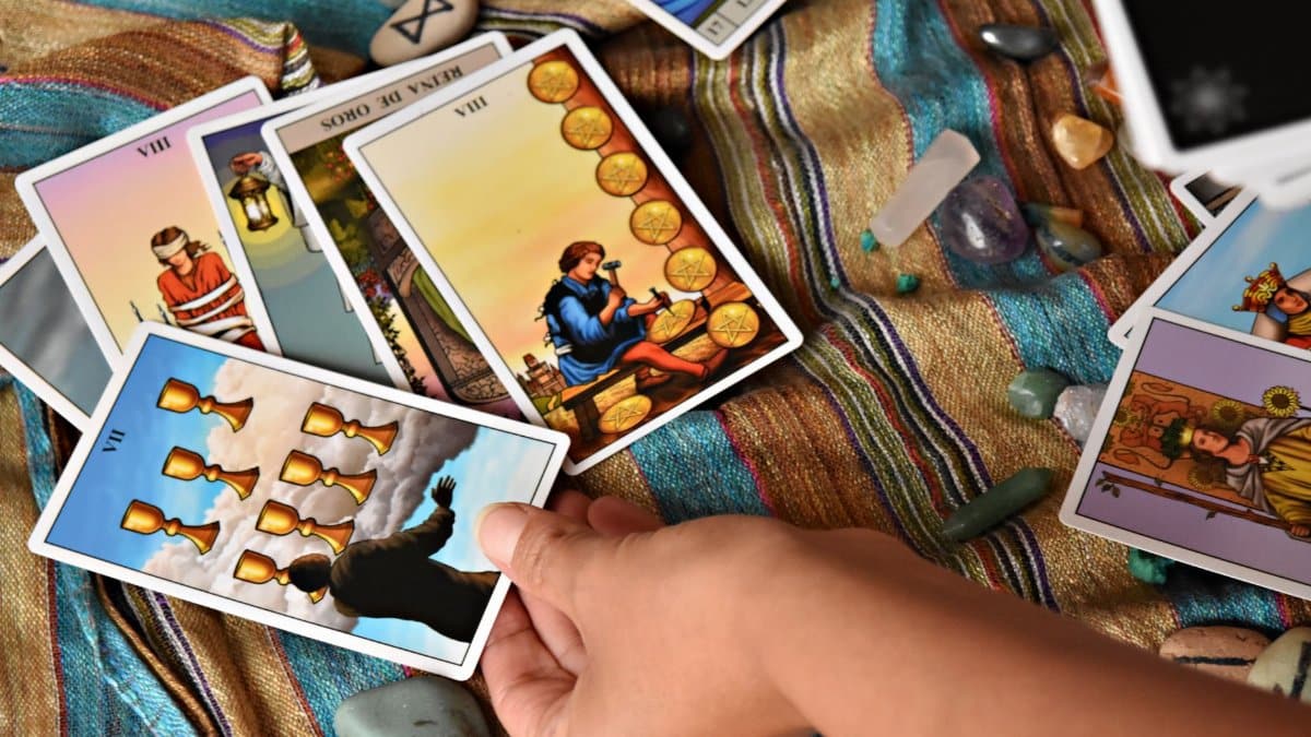 Person holding a tarot card amidst a spiritual setup with crystals and stones for a tarot reading session.