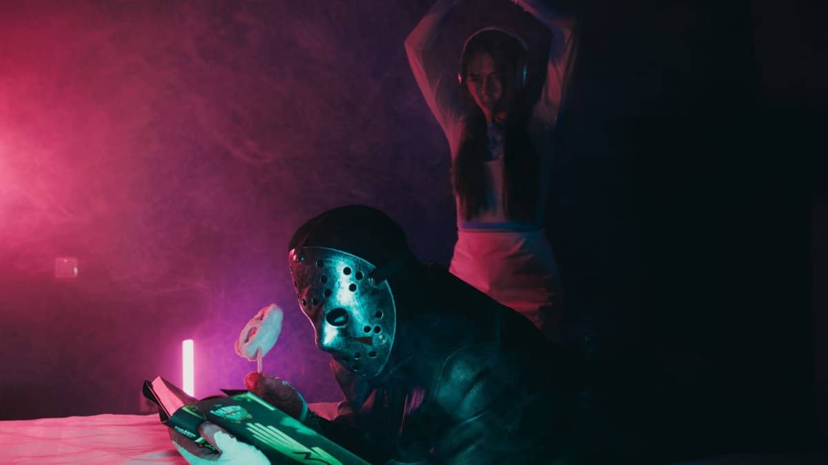 A dramatic scene with a masked figure reading under colorful neon lights.