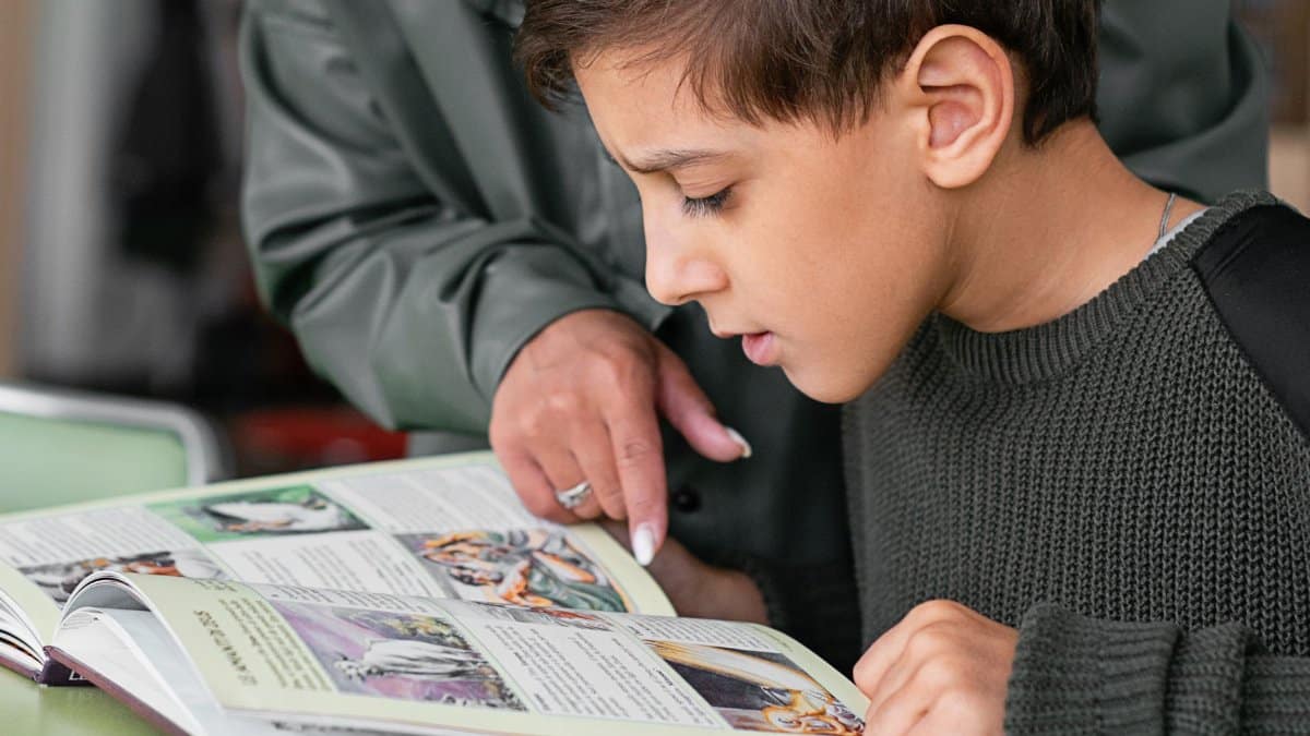 Boy concentrating on reading as adult points out text in a book.