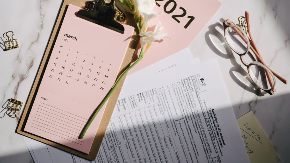Stylish office setup with March 2021 calendar, flower, tax form, and reading glasses on desk.
