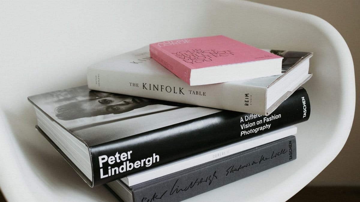 Arranged pile of modern art and fashion books from home collection placed on white chair near wall in modern light apartment