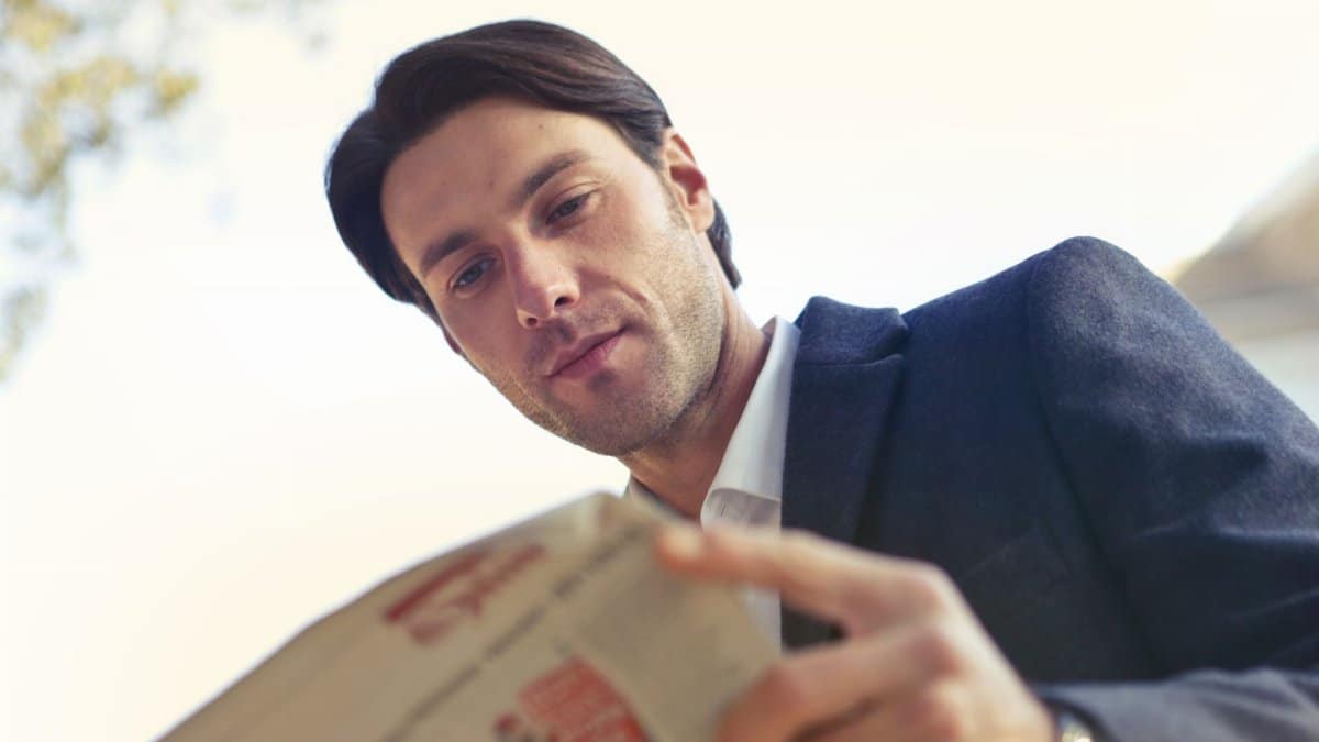 Adult man in formal attire reading a newspaper outdoors in Rome, Italy, during the day.