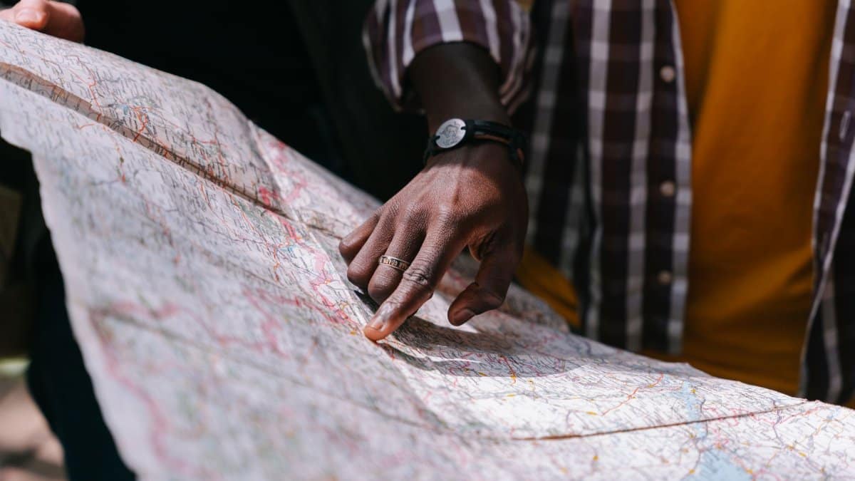 Close-up of a hand pointing at a detailed map, outdoors, wearing a striped shirt.