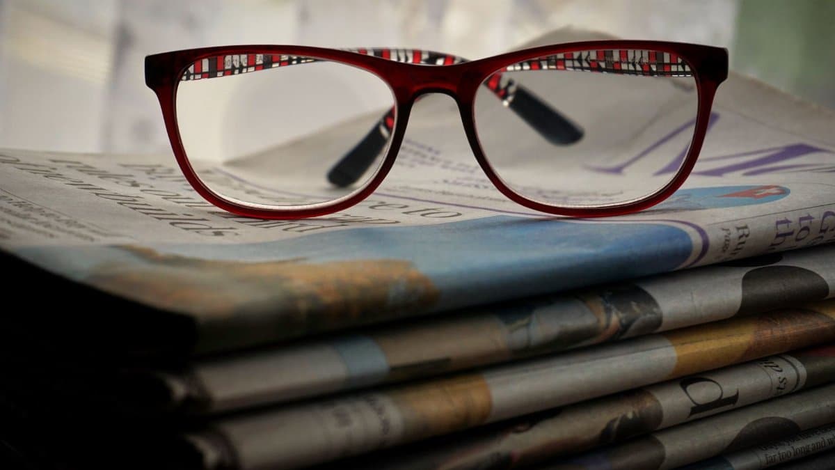 Close-up of red glasses resting on stacked newspapers, emphasizing reading and vision.