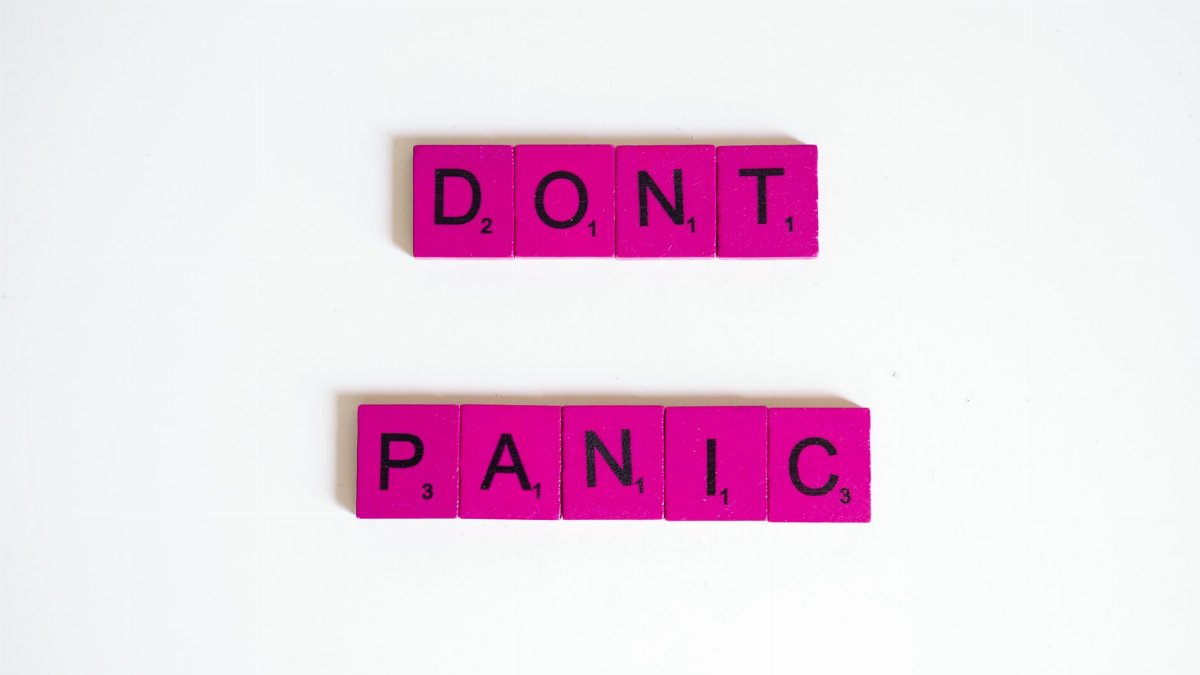 Pink Scrabble tiles spell out 'Don't Panic' on a white background.