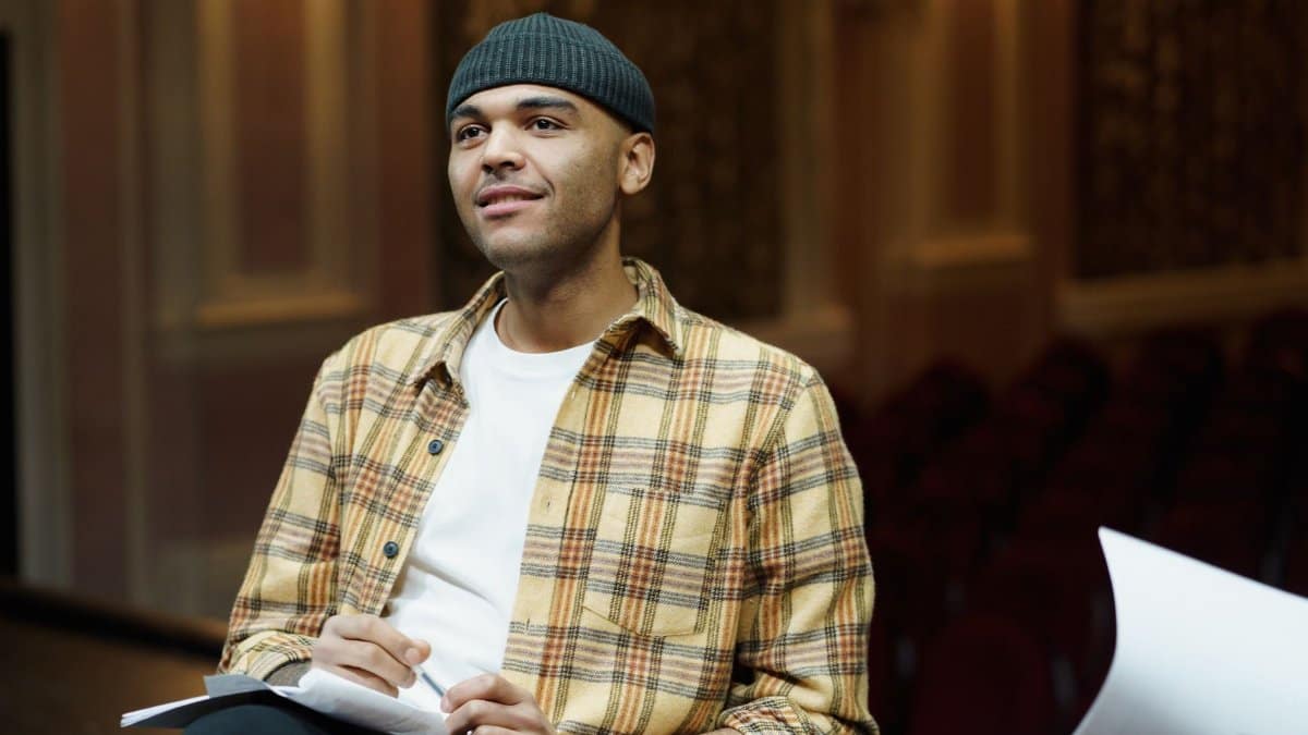Man in a theater reviewing script, wearing plaid shirt and knit cap