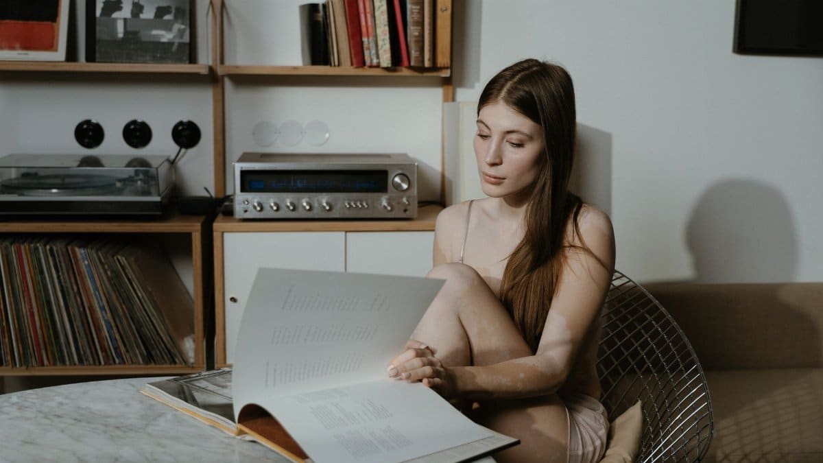 A young woman enjoys reading a book in a stylish and cozy indoor setting with a retro aesthetic.