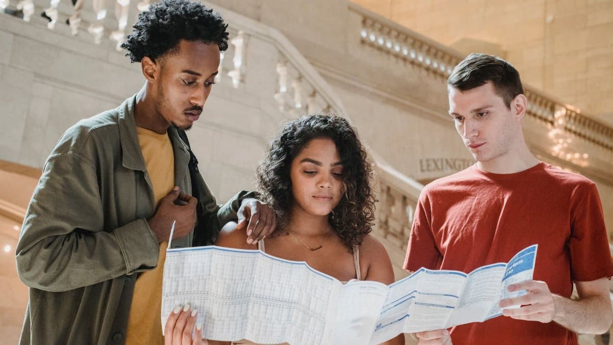 Low angle of concentrated young multiracial students reading map while searching for route in Grand Central Station in New York