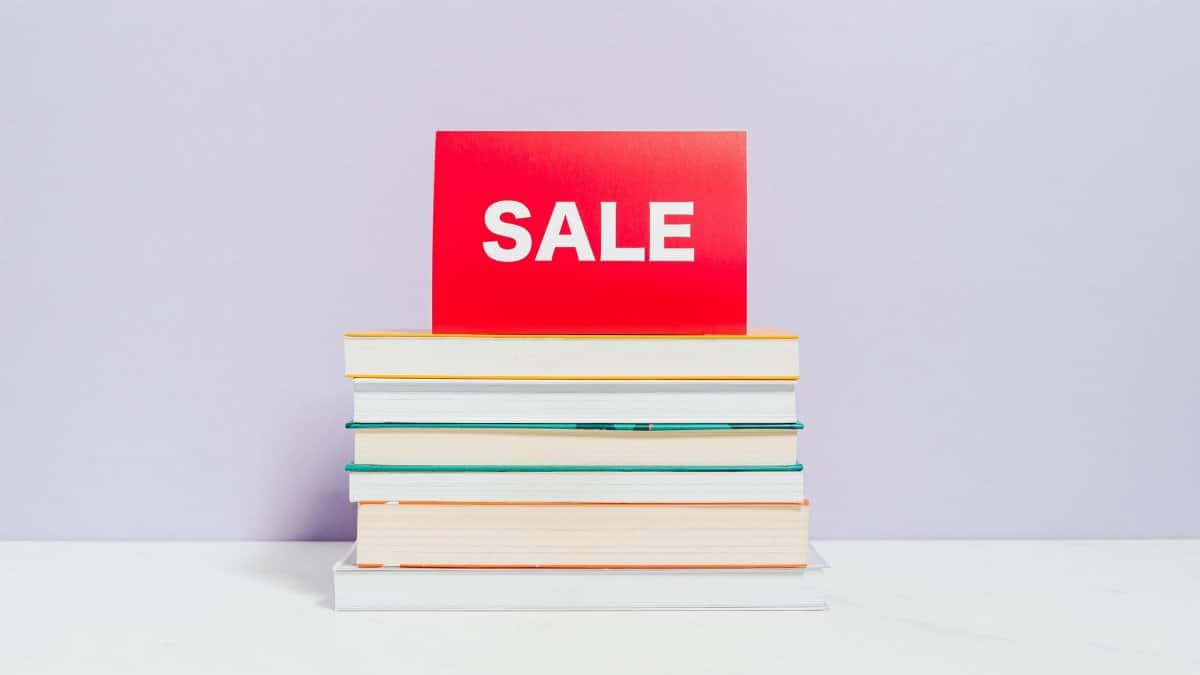 A stack of books with a red sale sign, ideal for promotions and bookshop advertisements.