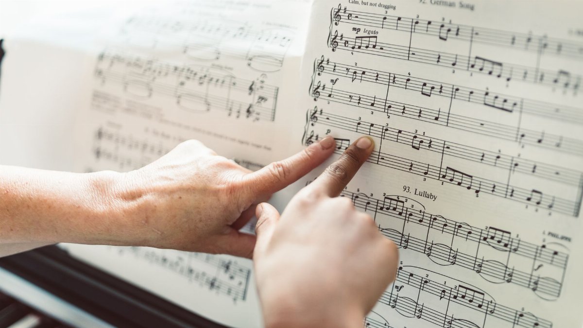 Close-up of hands pointing to notes on a music sheet during a piano lesson, highlighting music education.