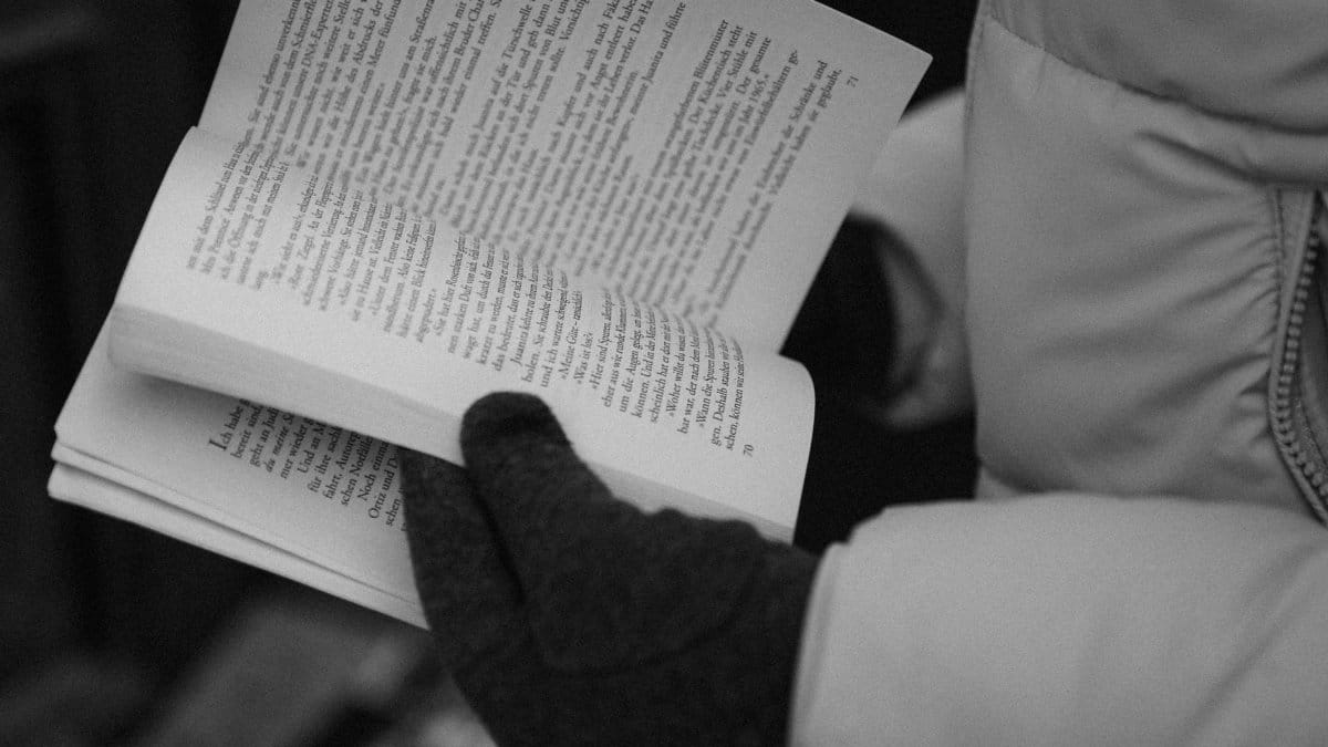 Close-up of gloved hands reading a book in black and white, emphasizing literature and cozy winter vibes.