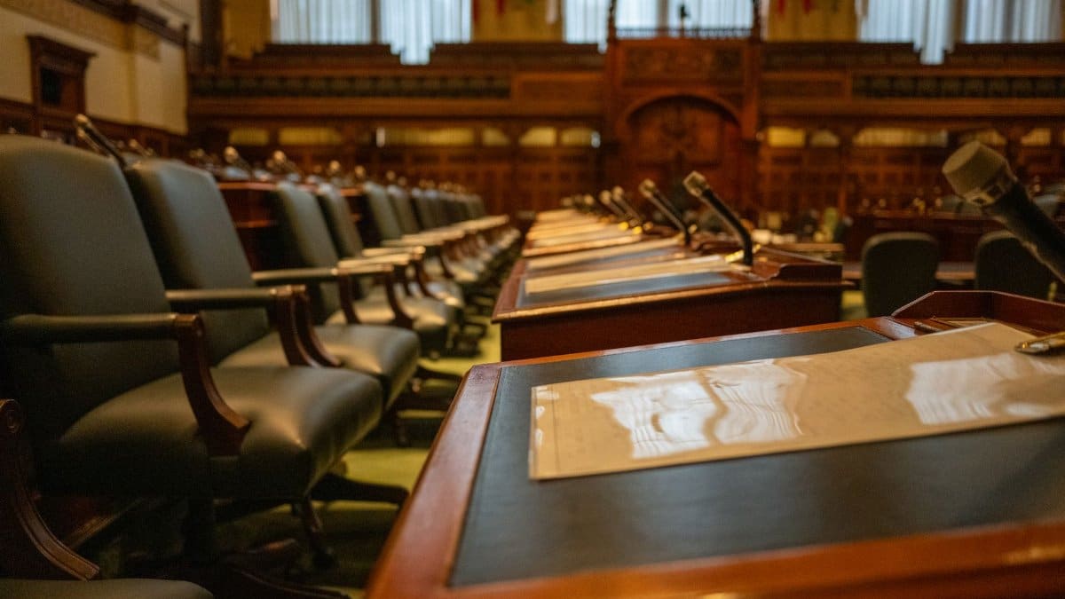 A detailed view of an empty legislative chamber with rows of desks and microphones, evoking governance.