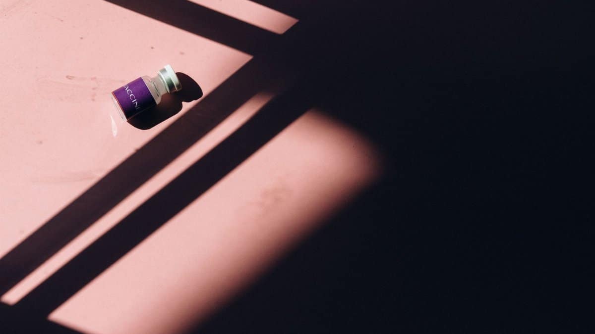 An artistic photograph of a vaccine vial amidst striking light and shadow patterns, emphasizing healthcare themes.