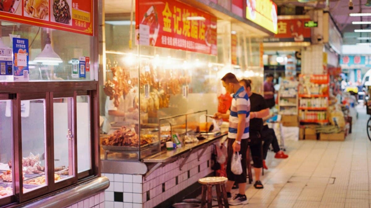 Man browsing food options at busy indoor street market stall.