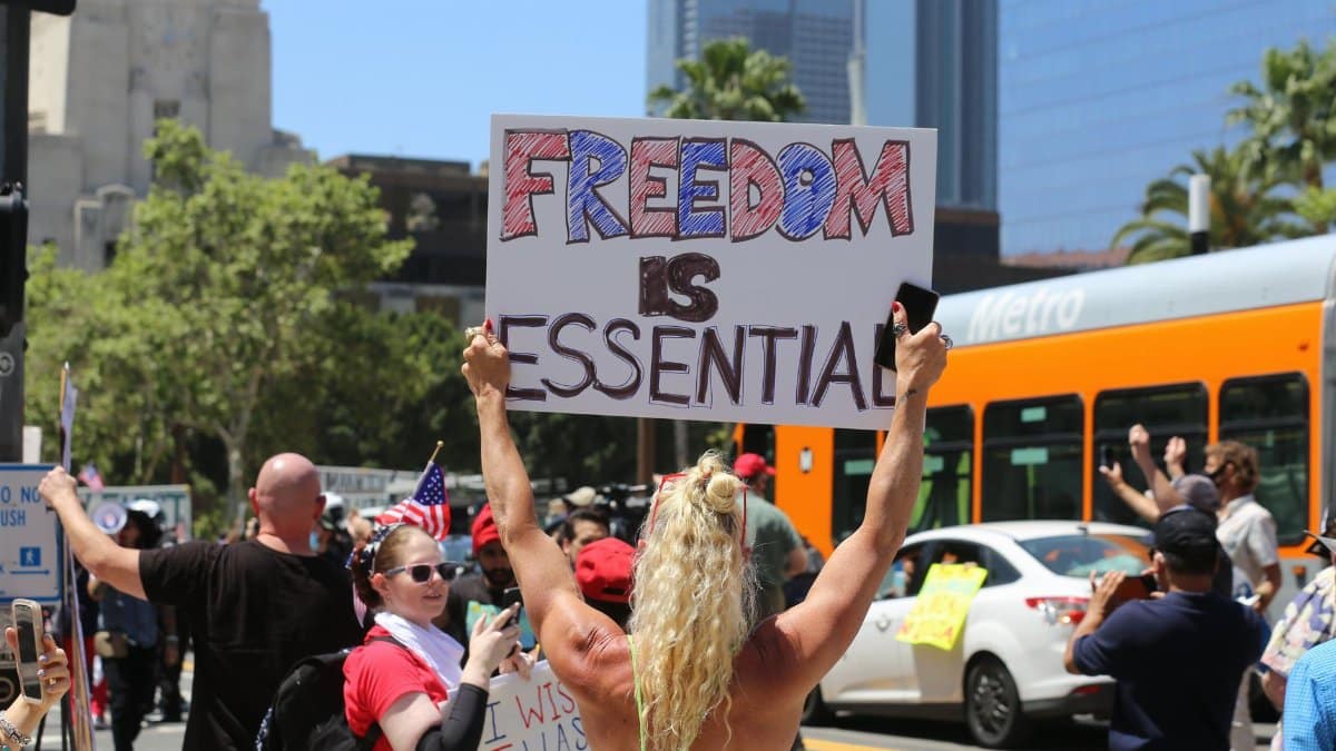 A protester holds a 'Freedom is Essential' sign during a city rally, advocating for social issues.