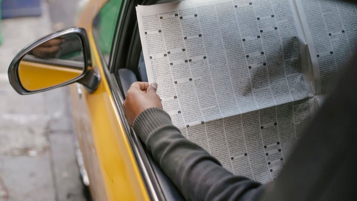 Crop unrecognizable person reading daily newspaper while sitting in car with opened window