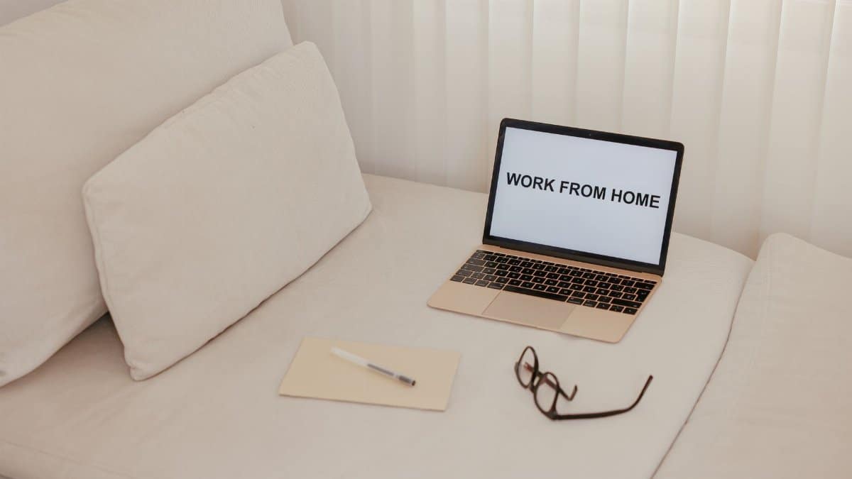 Minimalist workspace on a bed featuring a laptop, notepad, and glasses for remote work.