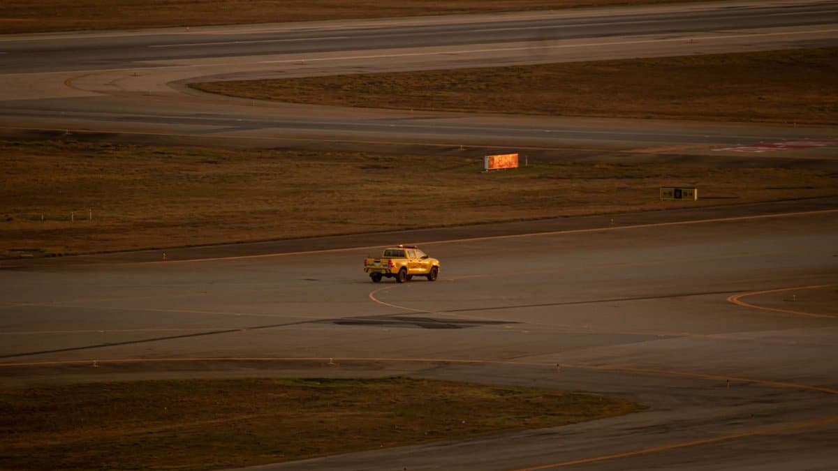 A yellow pickup truck drives across the open runway at Guarulhos International Airport.