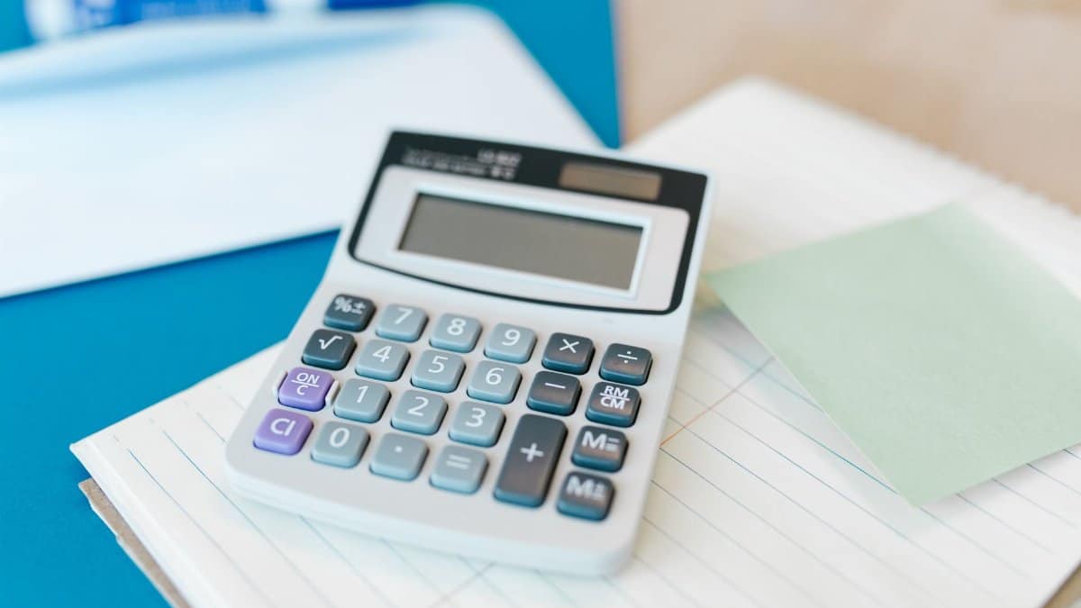 A white calculator on a stack of lined paper with a blue folder, capturing an office setting.