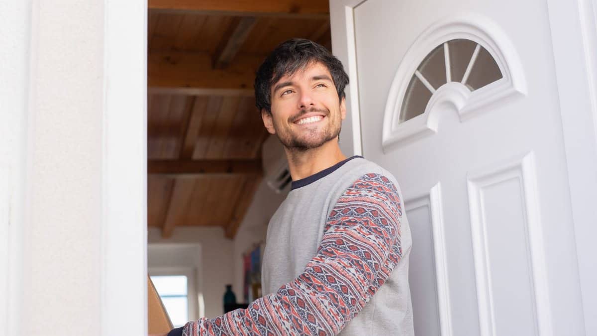 Happy man standing in doorway, smiling brightly. Indoor home setting, warm atmosphere.