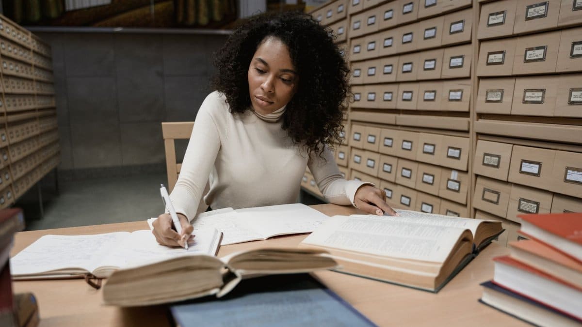 Woman taking notes in a library with books and a card catalog for research purposes.