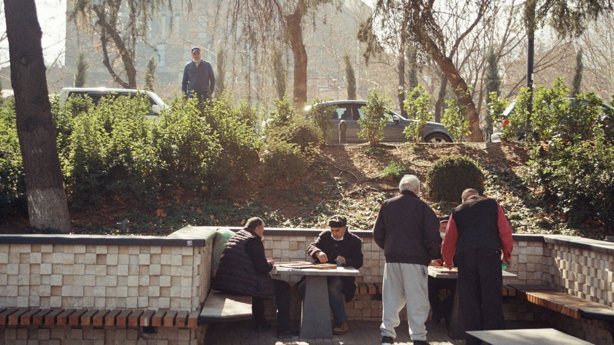 Men playing board games at outdoor park tables on a sunny day.