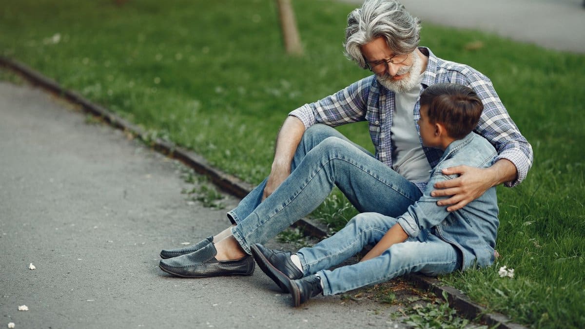 A grandfather and grandson sitting on a park curb, sharing a warm moment outdoors.