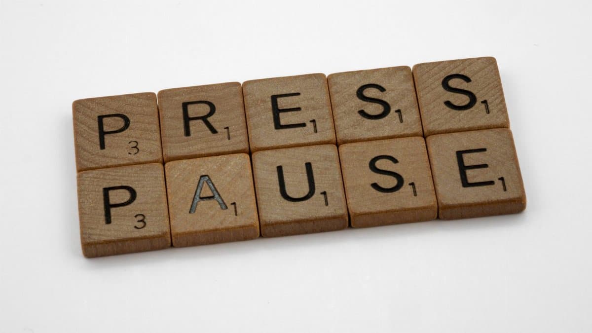 Wooden Scrabble tiles spelling 'Press Pause' on a white background.