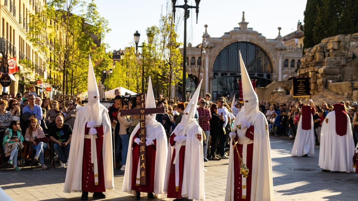 Adults in traditional capirotes during a Zaragoza Holy Week procession, a vibrant cultural event.