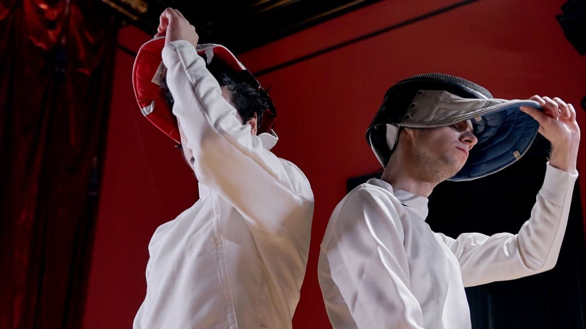 Two fencers removing their masks after an intense competition indoors.