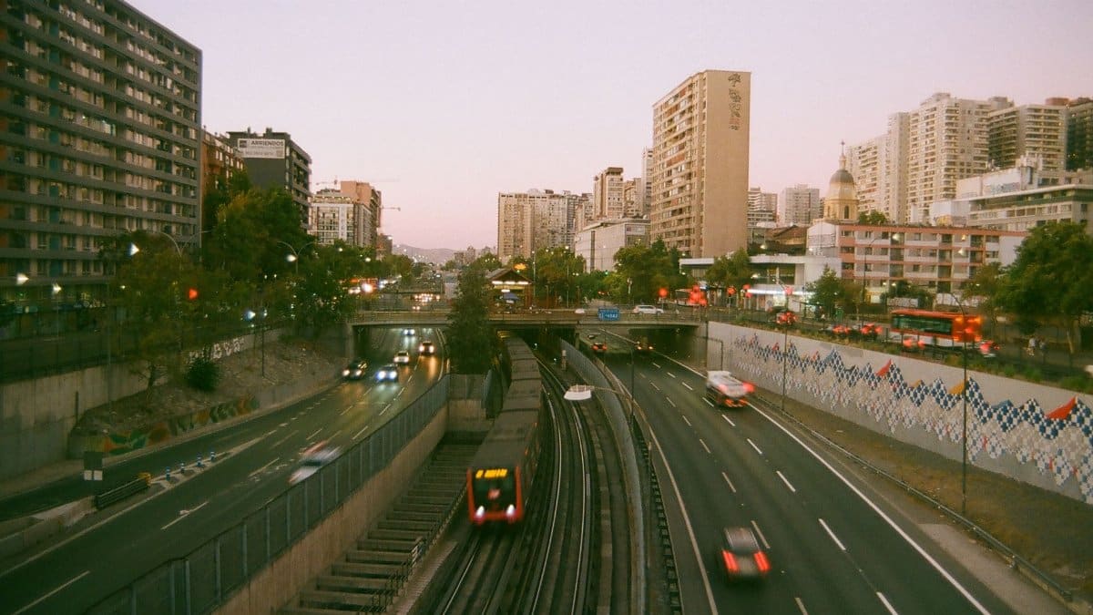 Santiago cityscape at sunset, featuring busy roads with cars and high-rise buildings under a warm sky.