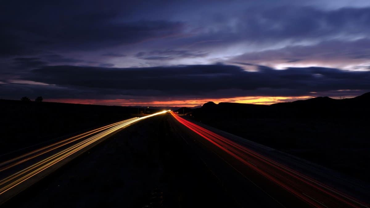 Long exposure photo of a highway at night with vibrant light trails and dramatic clouds.