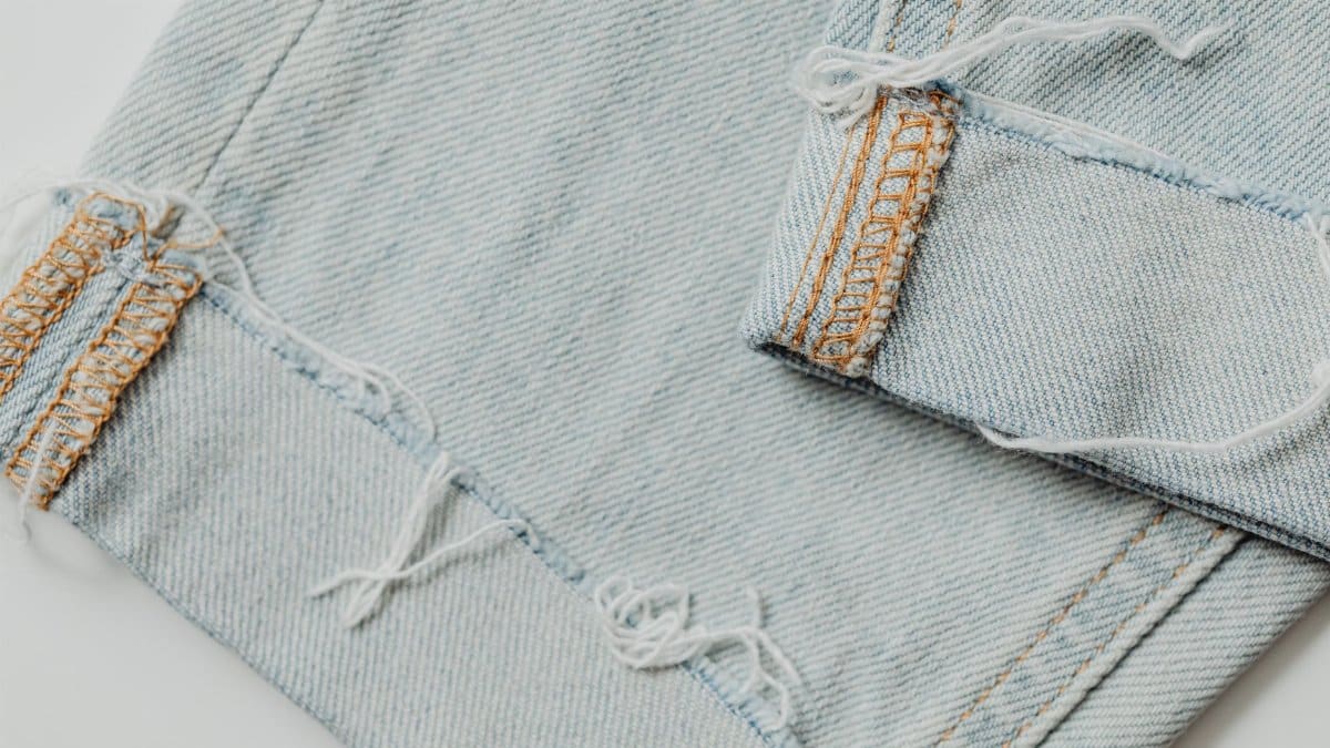 A detailed close-up shot of frayed light blue denim fabric displaying intricate stitching and texture.