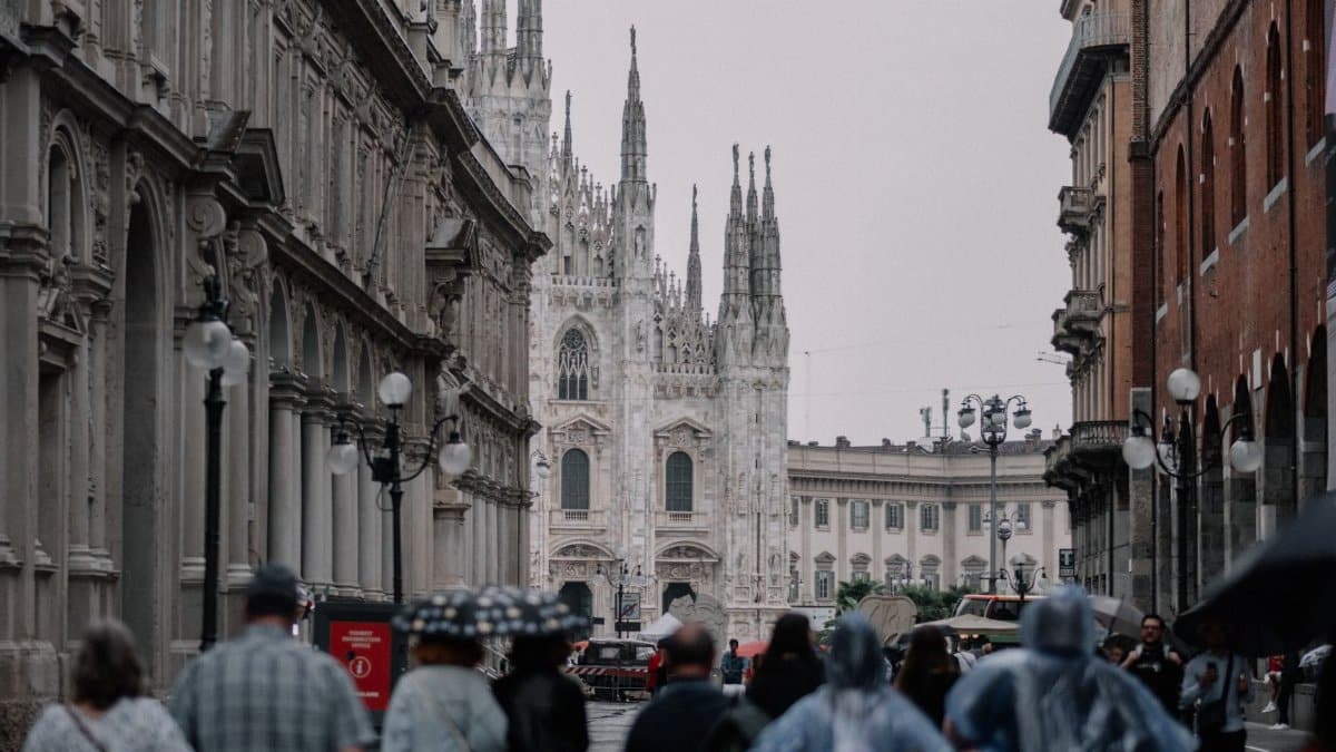 A rainy day scene capturing people walking near the iconic Milan Cathedral in Italy's historic city center.