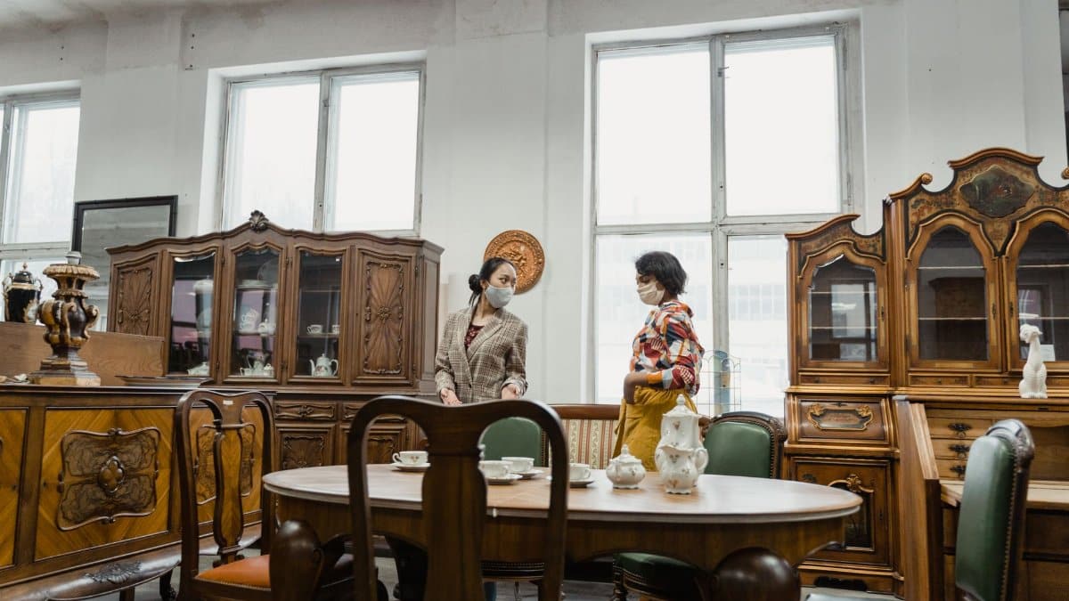 Two people in an antique furniture store, browsing elegant wooden pieces.